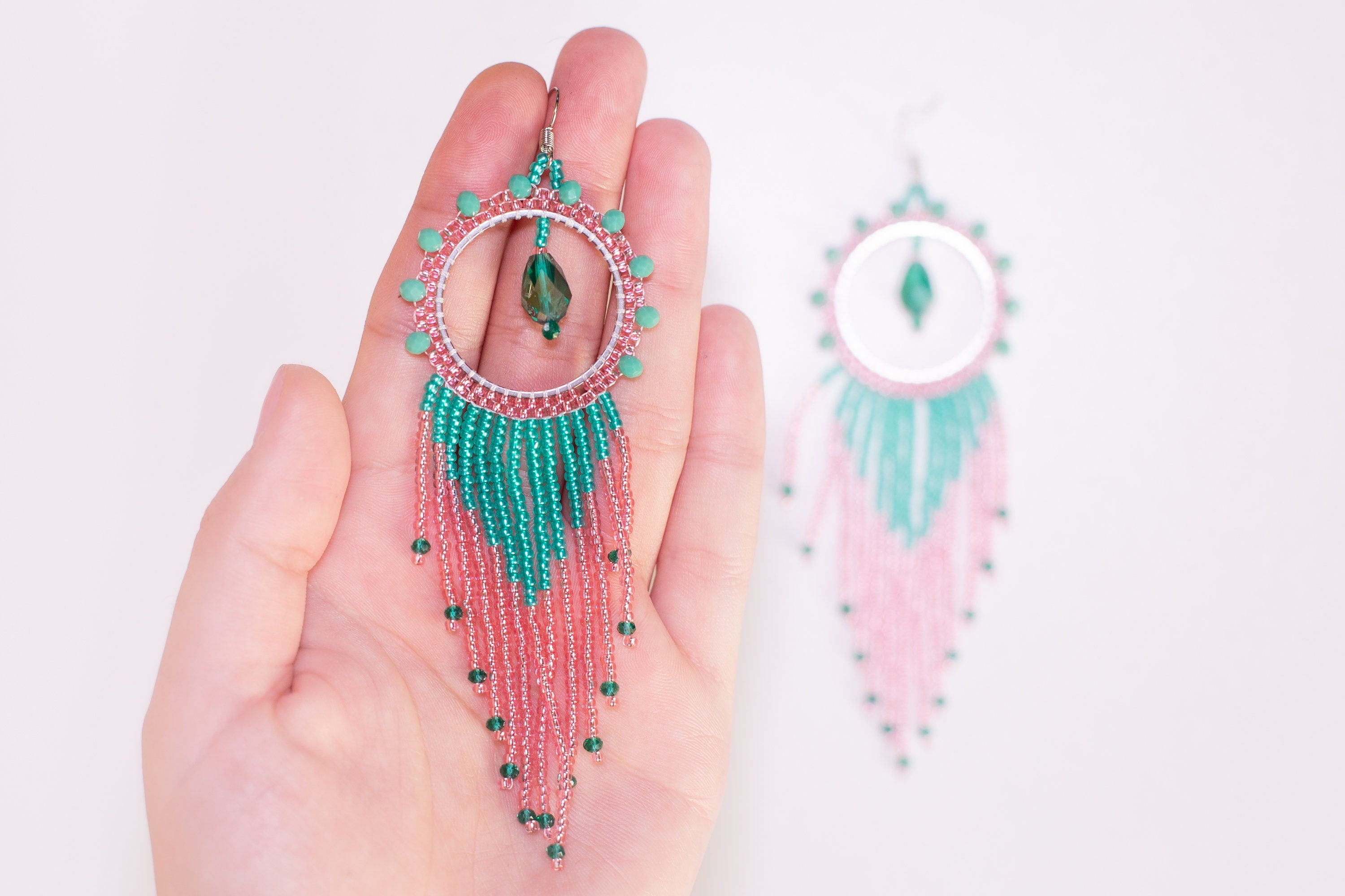 a pair of pink and green beaded earrings hanging from a tree branch